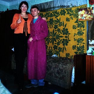 Two people standing together in a room with a tapestry.