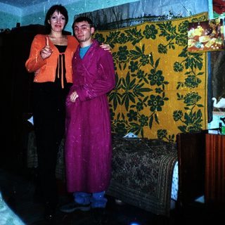 Two people standing together in a room with a tapestry.