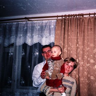 A couple holds a baby in their living room.