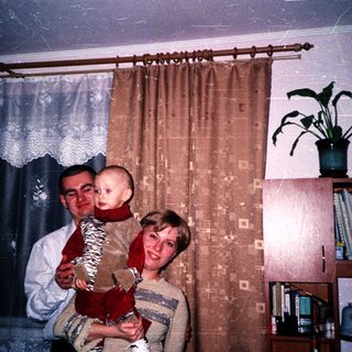 A couple holds a baby in their living room.