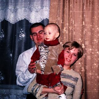 A couple holds a baby in their living room.