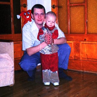 Man kneels, holding a toddler in a red outfit.