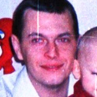 Man kneels, holding a toddler in a red outfit.