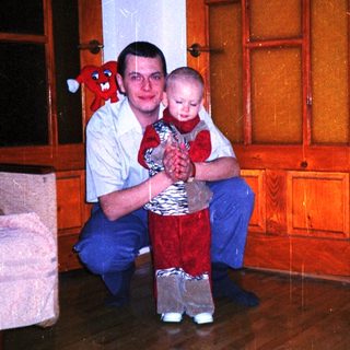 Man kneels, holding a toddler in a red outfit.