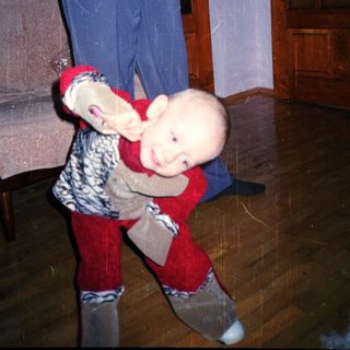 Baby playfully clinging to a person's legs indoors.