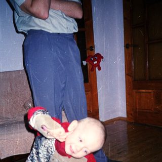 Baby playfully clinging to a person's legs indoors.