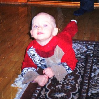 Baby crawls on a rug with a man in the background.