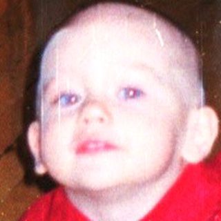 Baby crawls on a rug with a man in the background.
