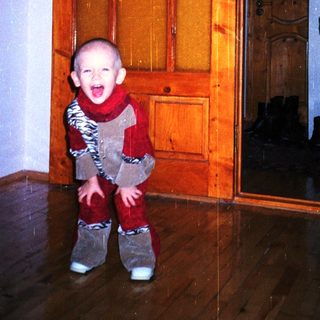 Baby wearing a patterned suit stands near a door.