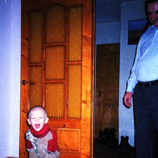 Baby wearing a patterned suit stands near a door.