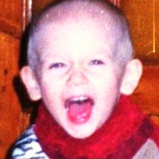 Baby wearing a patterned suit stands near a door.