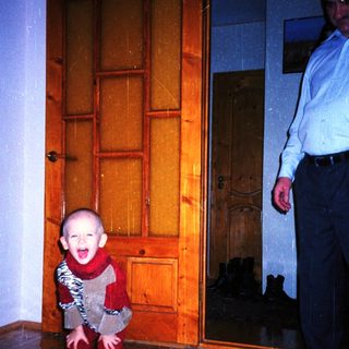 Baby wearing a patterned suit stands near a door.
