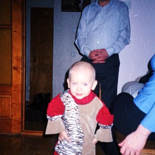 Baby standing, held by an adult, in a home.