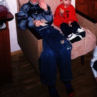 Three boys in overalls sit and stand in a room.