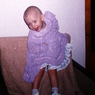 Child with a shaved head sits on a chair.
