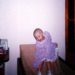 Child with a shaved head sits on a chair.