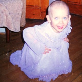 Here's a brief summary of the image: Young child with a shaved head kneels near a door.