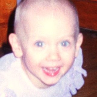 Here's a brief summary of the image: Young child with a shaved head kneels near a door.