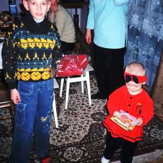 Here's a brief summary of the image: Boy and toddler in patterned clothing stand with a woman.