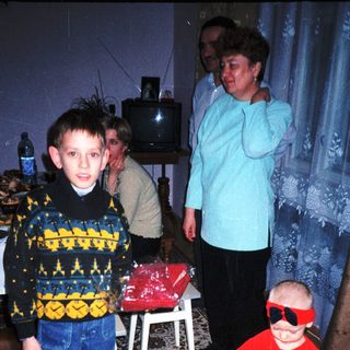 Here's a brief summary of the image: Boy and toddler in patterned clothing stand with a woman.