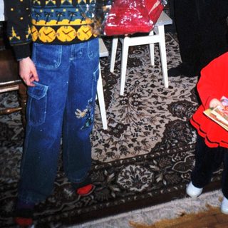 Here's a brief summary of the image: Boy and toddler in patterned clothing stand with a woman.