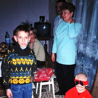 Here's a brief summary of the image: Boy and toddler in patterned clothing stand with a woman.