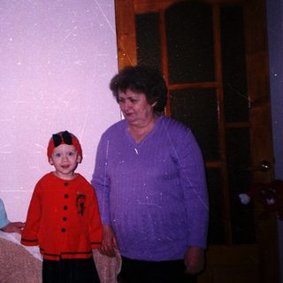 Child in costume stands with an adult near a door.