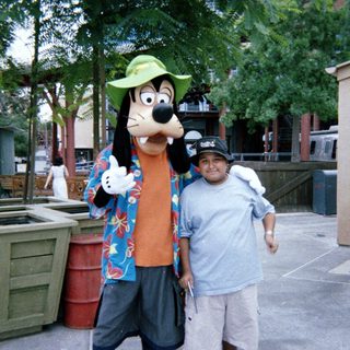 Man posing for photo with Goofy character at Disney.