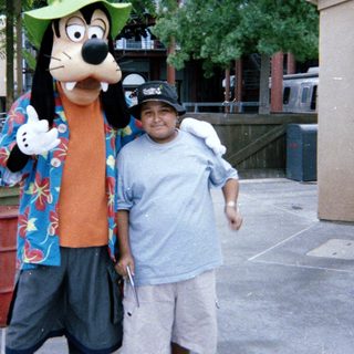 Man posing for photo with Goofy character at Disney.