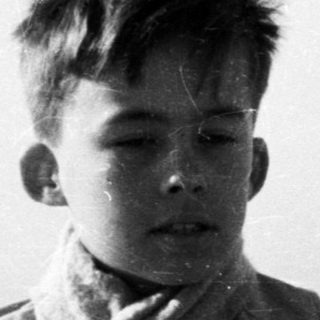 Young boy in coat stands near decorative railing.
