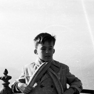 Young boy in coat stands near decorative railing.