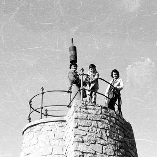 Three children stand atop a stone tower with a device.