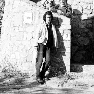 Two boys peer from a stone tower in a landscape.