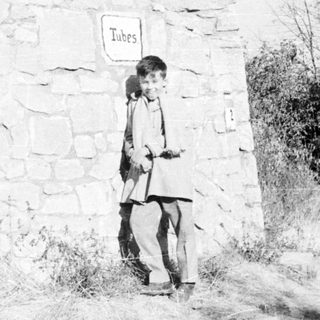 Boy stands near a stone wall with a "Tubes" sign.