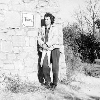 Man stands near a stone wall, holding coiled tubes.