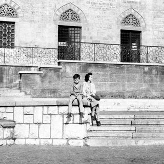 Two children sit on stone steps in a monochrome setting.