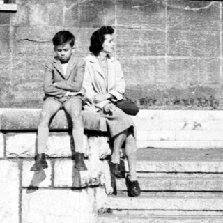 Two children sit on stone steps in a monochrome setting.
