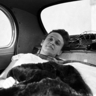 Man lies injured in a bed, covered with blankets.