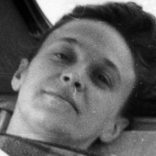 Man lies injured in a bed, covered with blankets.