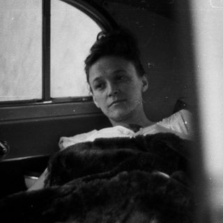 Here's a brief summary of the image: Woman in bed, looking out a window.