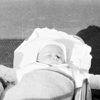 Infant sleeps in a vintage stroller, wrapped in blankets.