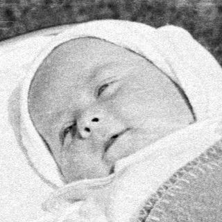 Baby in a pram, outdoors, wearing a bonnet.