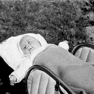 Baby in a pram, outdoors, wearing a bonnet.