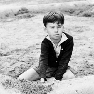 Boy sits in a dirt-lined, walled enclosure.