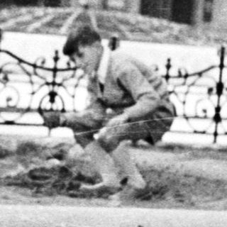 Two boys playing in a dirt area near a fence.