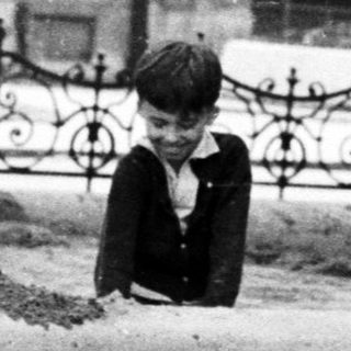 Two boys playing in a dirt area near a fence.