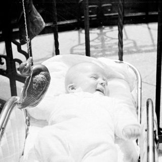 Baby in a pram, viewed through an ornate fence.
