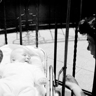 Baby in a pram, viewed through an ornate fence.