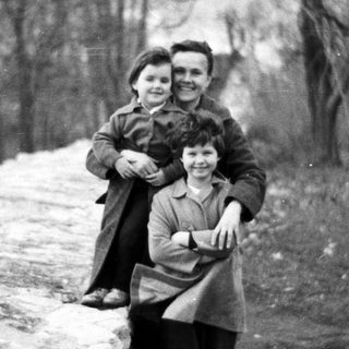 Two children pose on a stone wall outdoors.