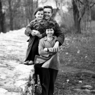 Two children pose on a stone wall outdoors.